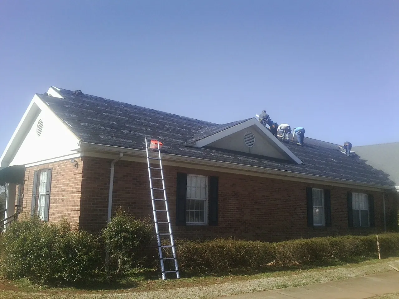 Crew tearing shingles off a brick ranch roof with a ladder set — Emergency Roof Repair work by our crew in Fidelity
