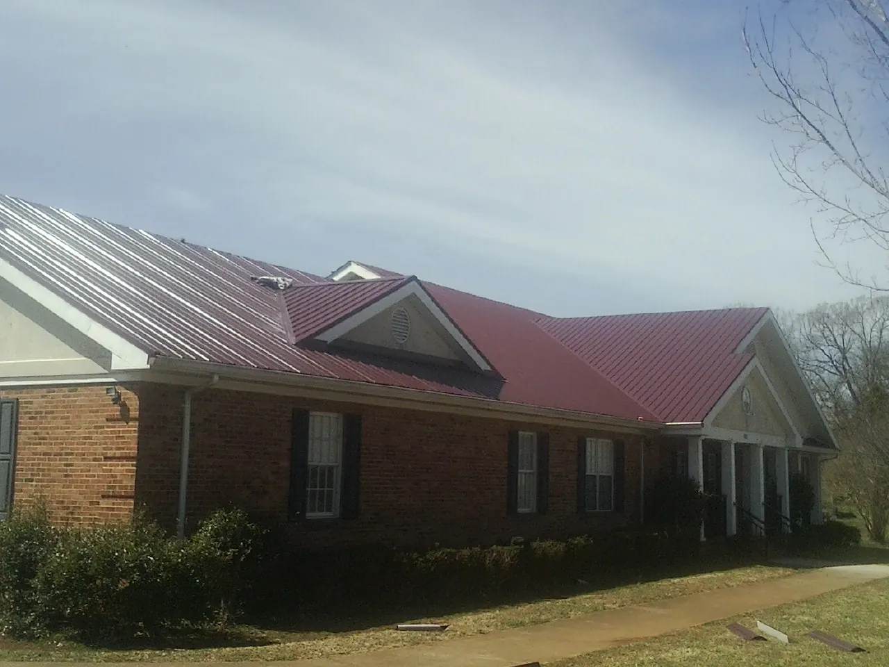 Red metal roof with gabled entries on a long brick building, from a Hail Damage Roof Repair job in Fidelity