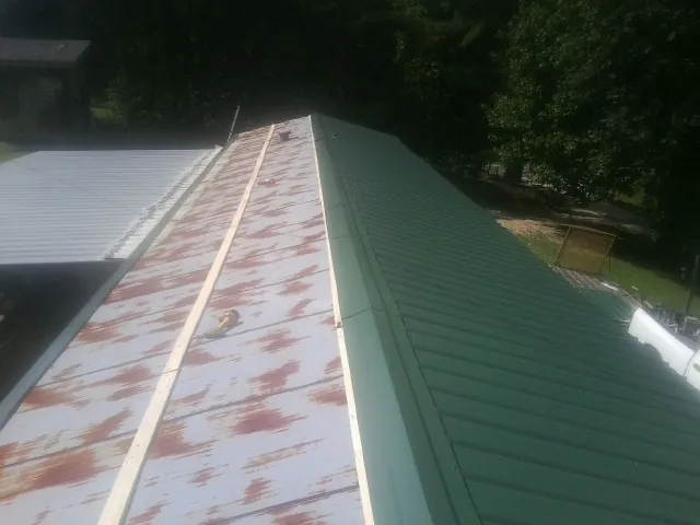 Old rusted panels beside newly installed green metal roofing — Wind Damage Roof Repair by Roofing Brothers in Fidelity