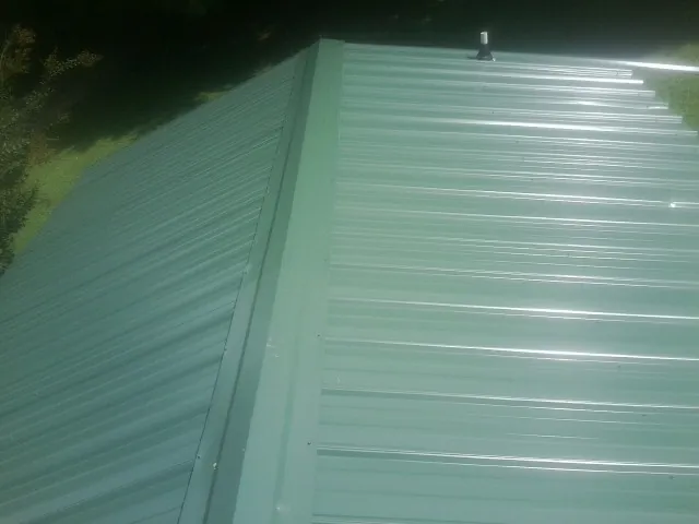 New green metal panels meeting at the ridge of a roof — Flat Roof Repair work by our crew in Fidelity