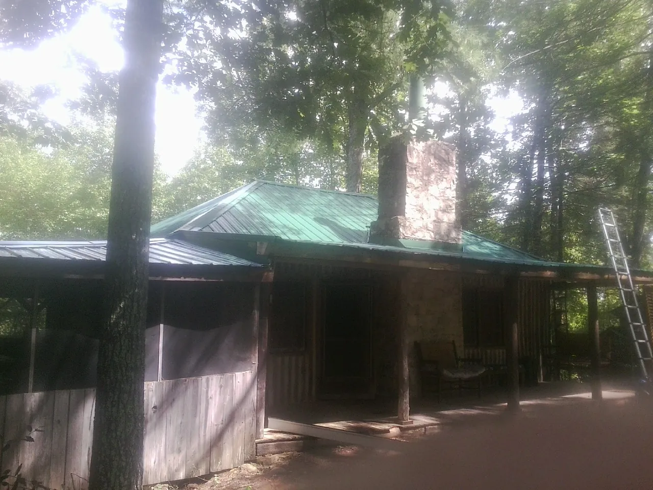 Green metal roof and stone chimney above a log cabin porch in Fidelity