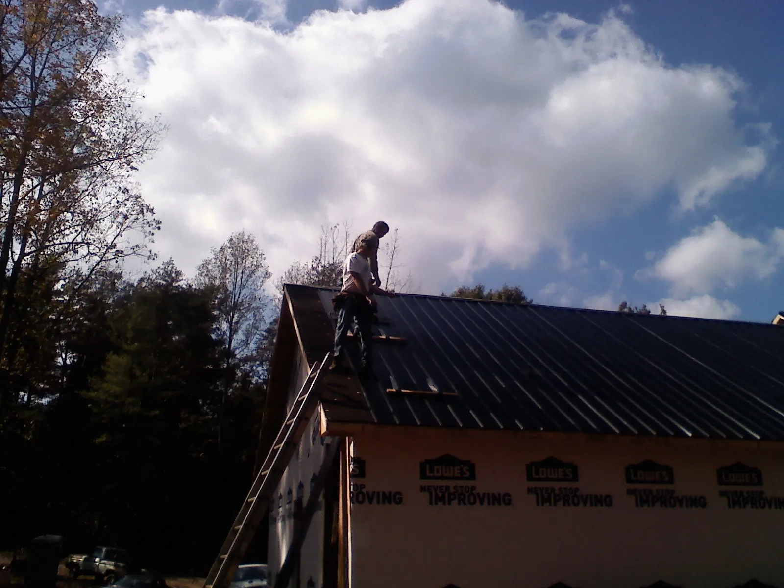Roofer fastening dark metal panels high against a cloudy sky, from a Roof Inspection job in Fidelity